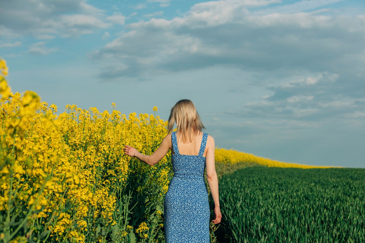 Blonde woman in blue dress in rapeseed field on blue sky background; Shutterstock ID 2303421033; purchase_order: MB images; job: ; client: ; other: 